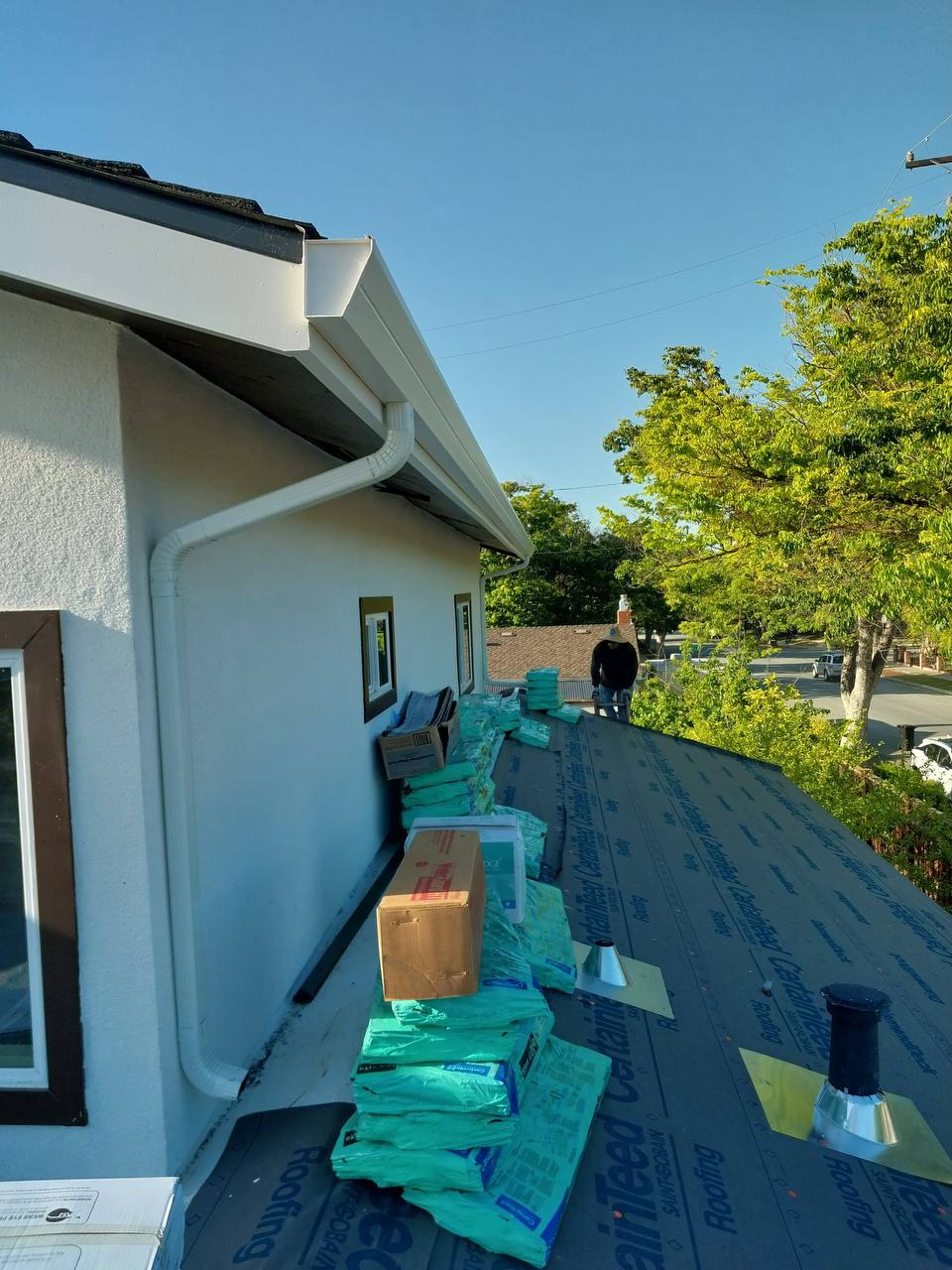 CertainTeed shingle bundles staged on underlayment along the eave during installation, with new gutter visible